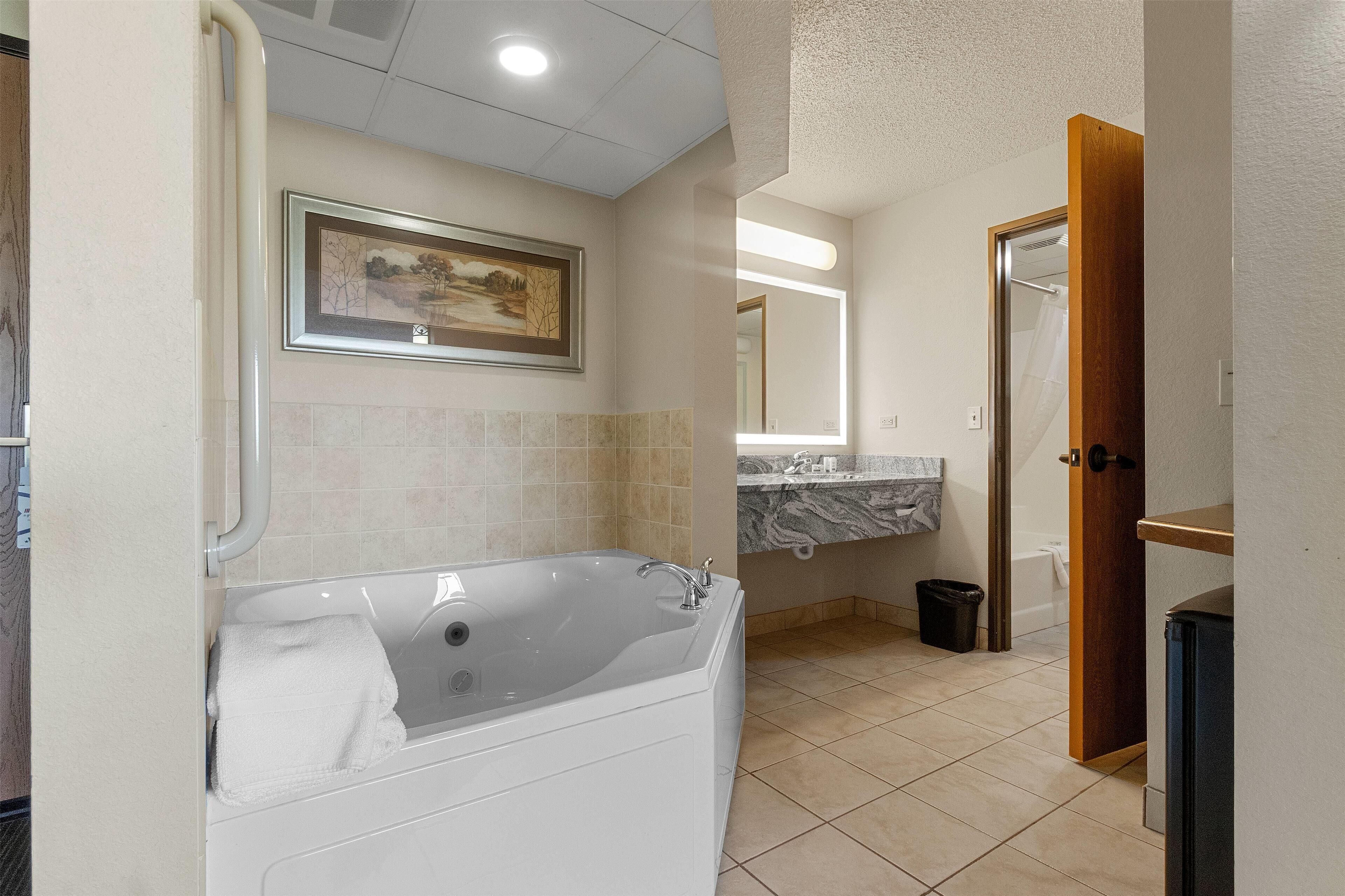 A modern bathroom with a large bathtub, a marble countertop, and a framed landscape painting on the wall.