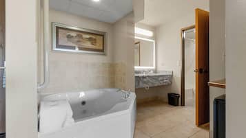 A modern bathroom with a large bathtub, a marble countertop, and a framed landscape painting on the wall.