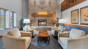 A cozy living room with a fireplace, comfortable seating, and decorative wall art. - AmericInn by Wyndham Green Bay East (Green Bay)