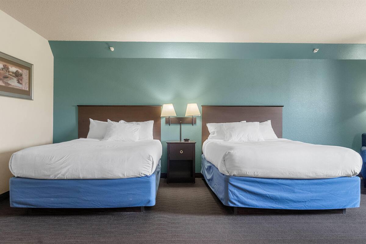 Ein Hotelzimmer mit zwei Betten, einem Nachttisch mit Lampen und einem Gemälde an der Wand.