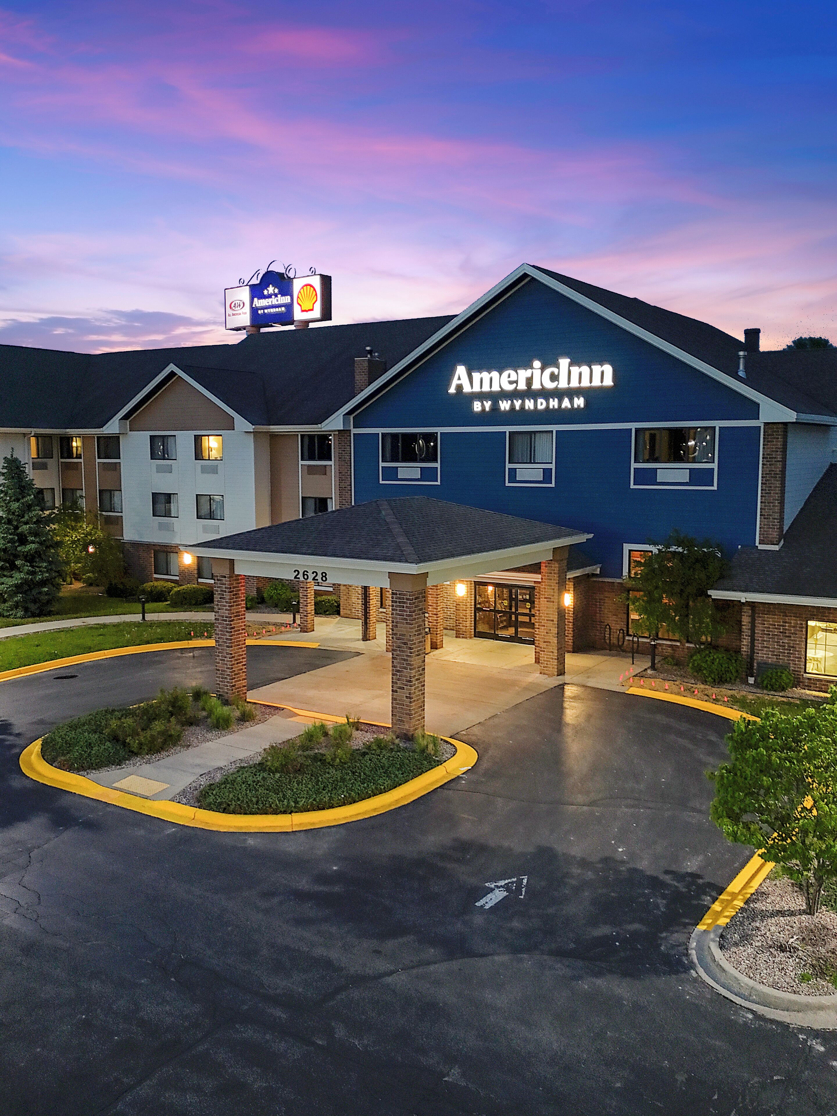 Ein American Inn by Wyndham mit überdachter Einfahrt, einem Shell-Tankstellenschild und einem Parkplatz.