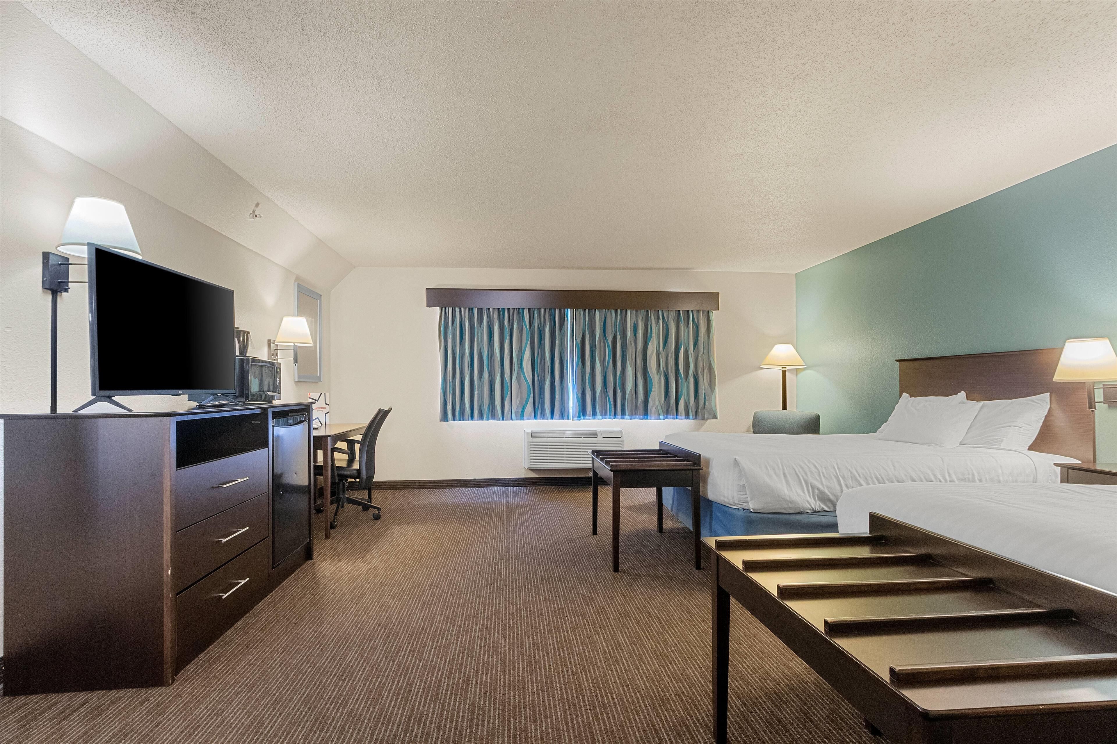 A hotel room with a bed, a desk with a television, a chair, a desk lamp, and a window with curtains.