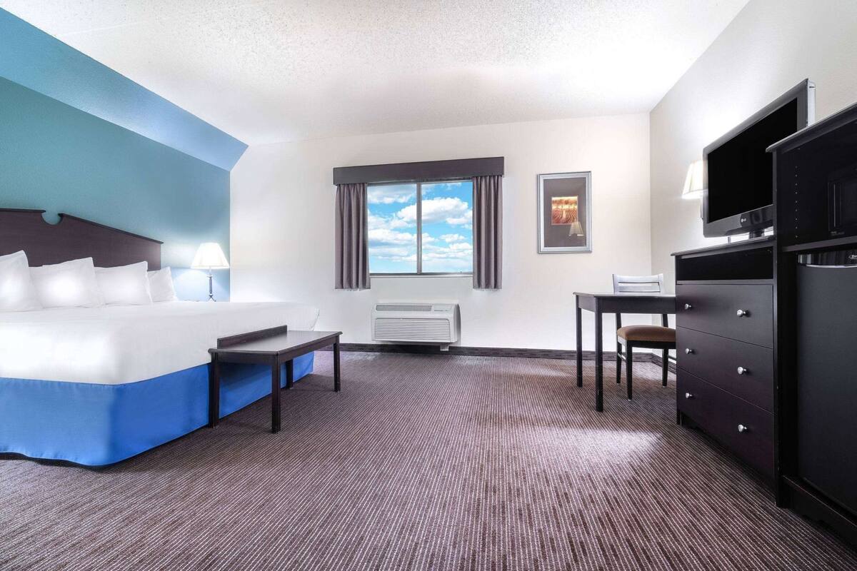 Ein Hotelzimmer mit einem Bett, einem Schreibtisch, einem Stuhl, einem Fernseher und einem Fenster mit Vorhängen.