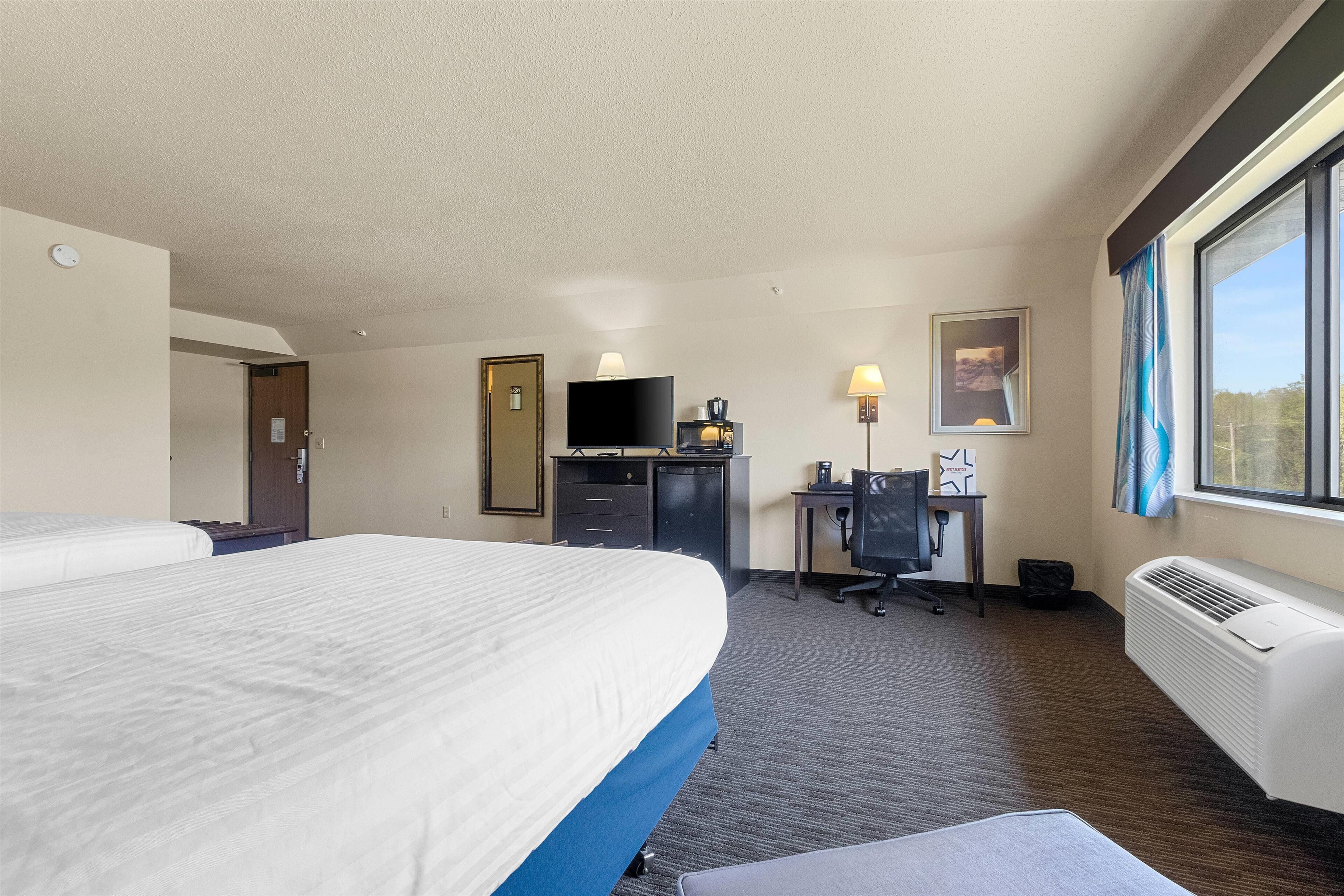 A hotel room with a large bed, a desk with a computer, a chair, a TV, and a window with curtains.
