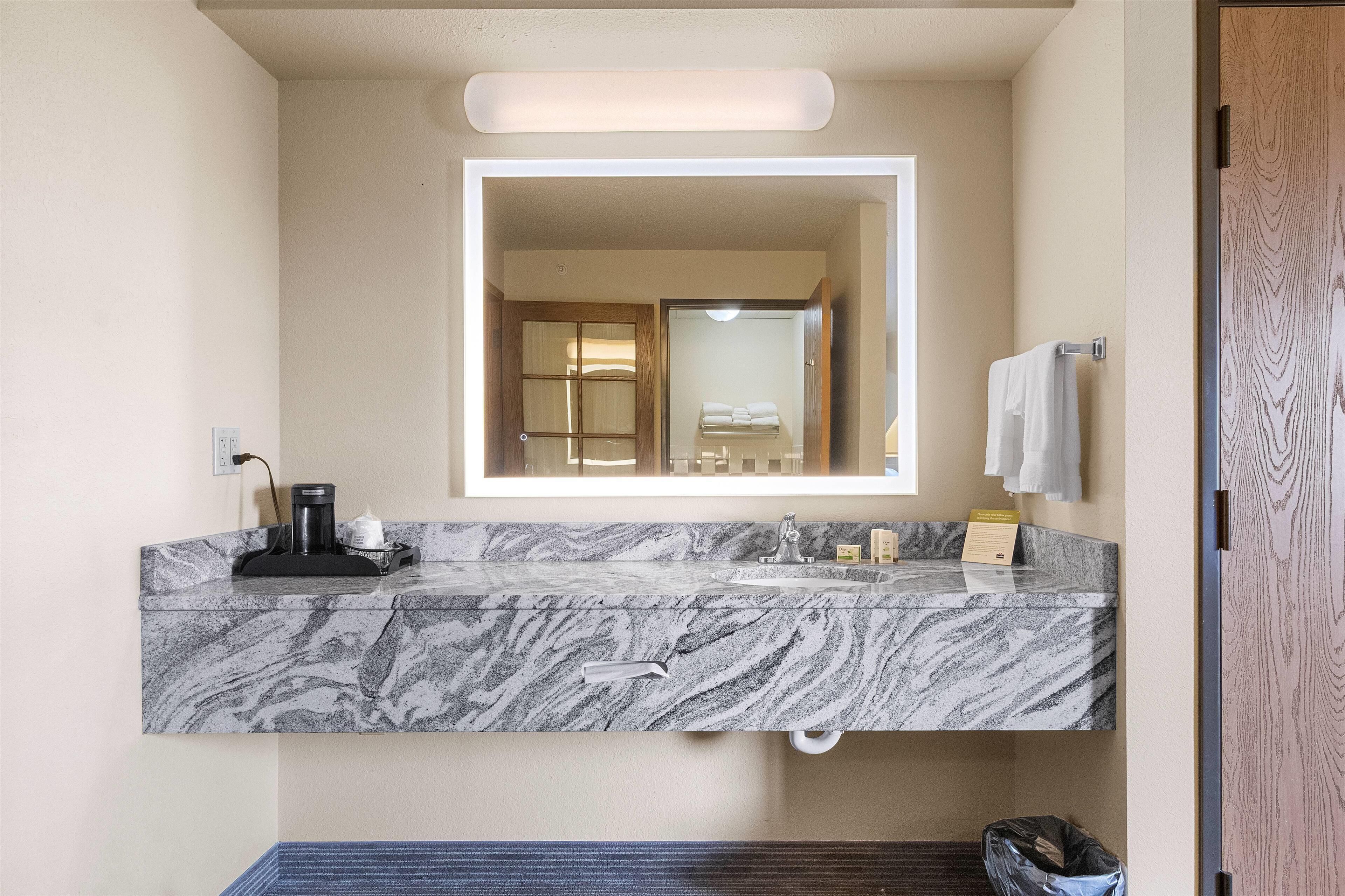 A bathroom with a marble sink, a mirror, a towel rack, and a trash bin.