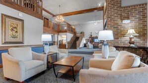 A spacious lobby with a high ceiling, wooden staircase, and a chandelier. There are multiple seating areas with sofas and a coffee table. - AmericInn by Wyndham Green Bay East (Green Bay)