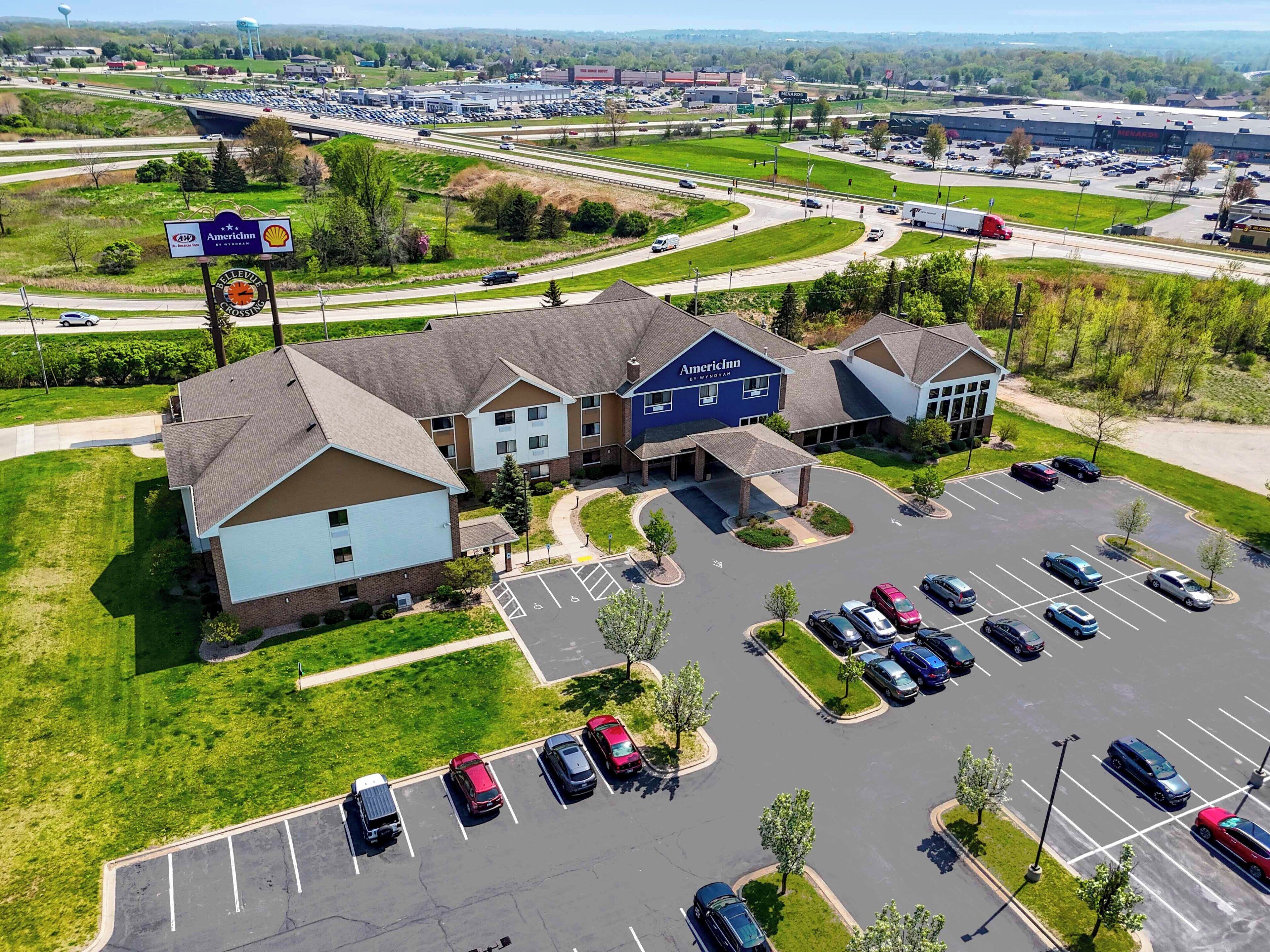 En vy från ovan av ett hotell med en parkeringsplats, en stor byggnad med skylten "AmericInn by Wyndham", och en motorväg i bakgrunden.