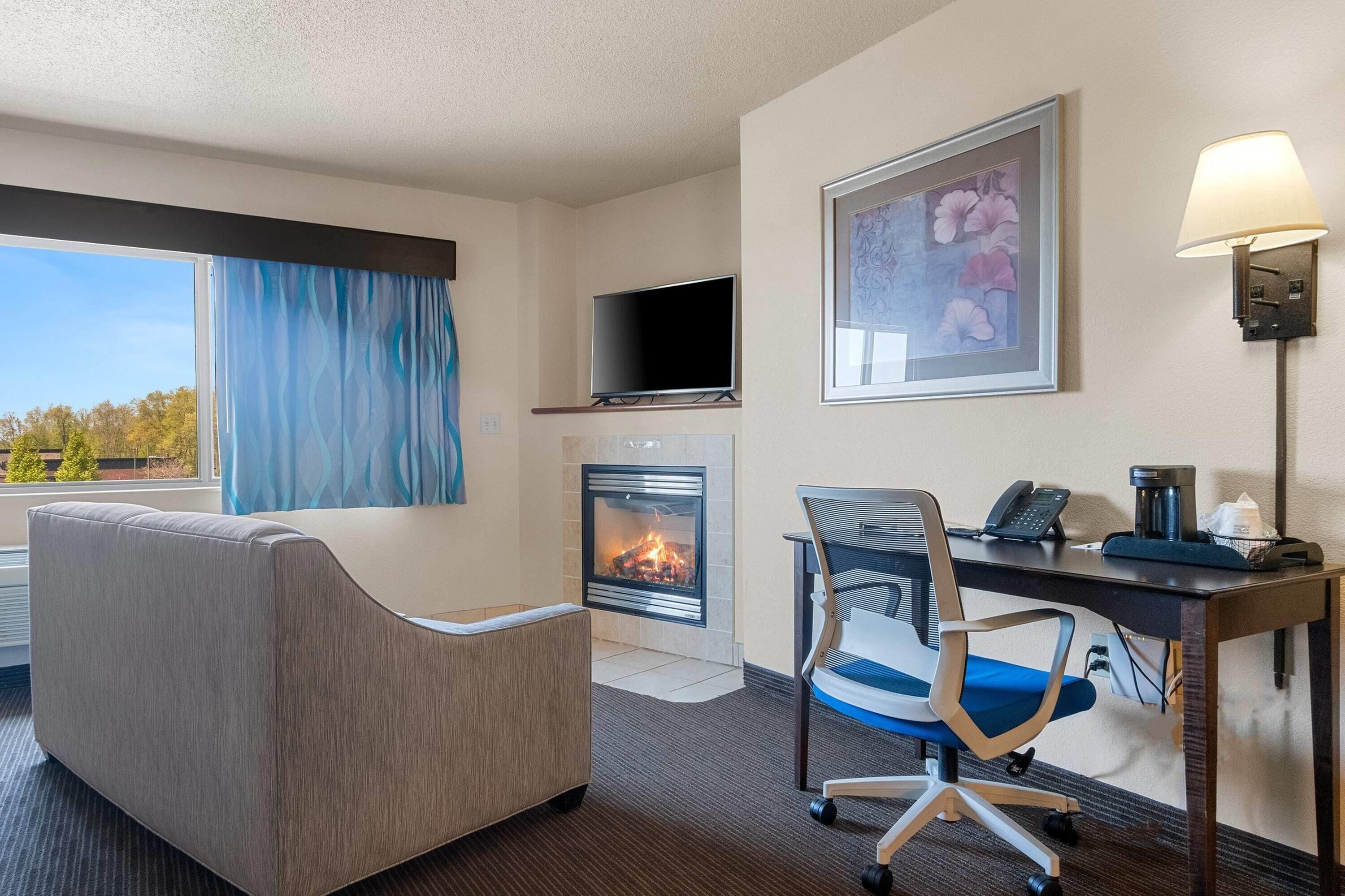 Een hotelkamer met een bank, een bureau met stoel, een open haard, een televisie en een schilderij aan de muur.