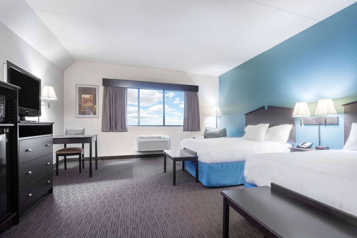 Ein Hotelzimmer mit zwei Betten, einem Schreibtisch, einem Stuhl, einem Fernseher und einem Fenster mit Vorhängen.