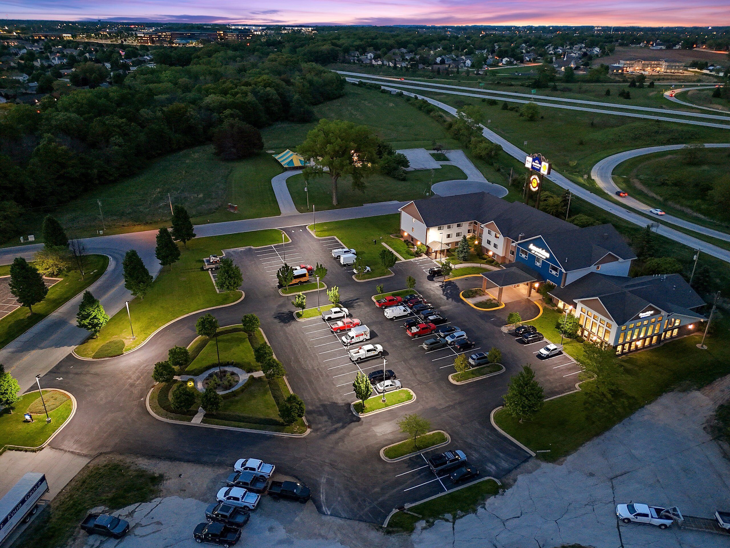 An aerial view of a hotel with a parking lot, multiple buildings, and surrounding greenery.