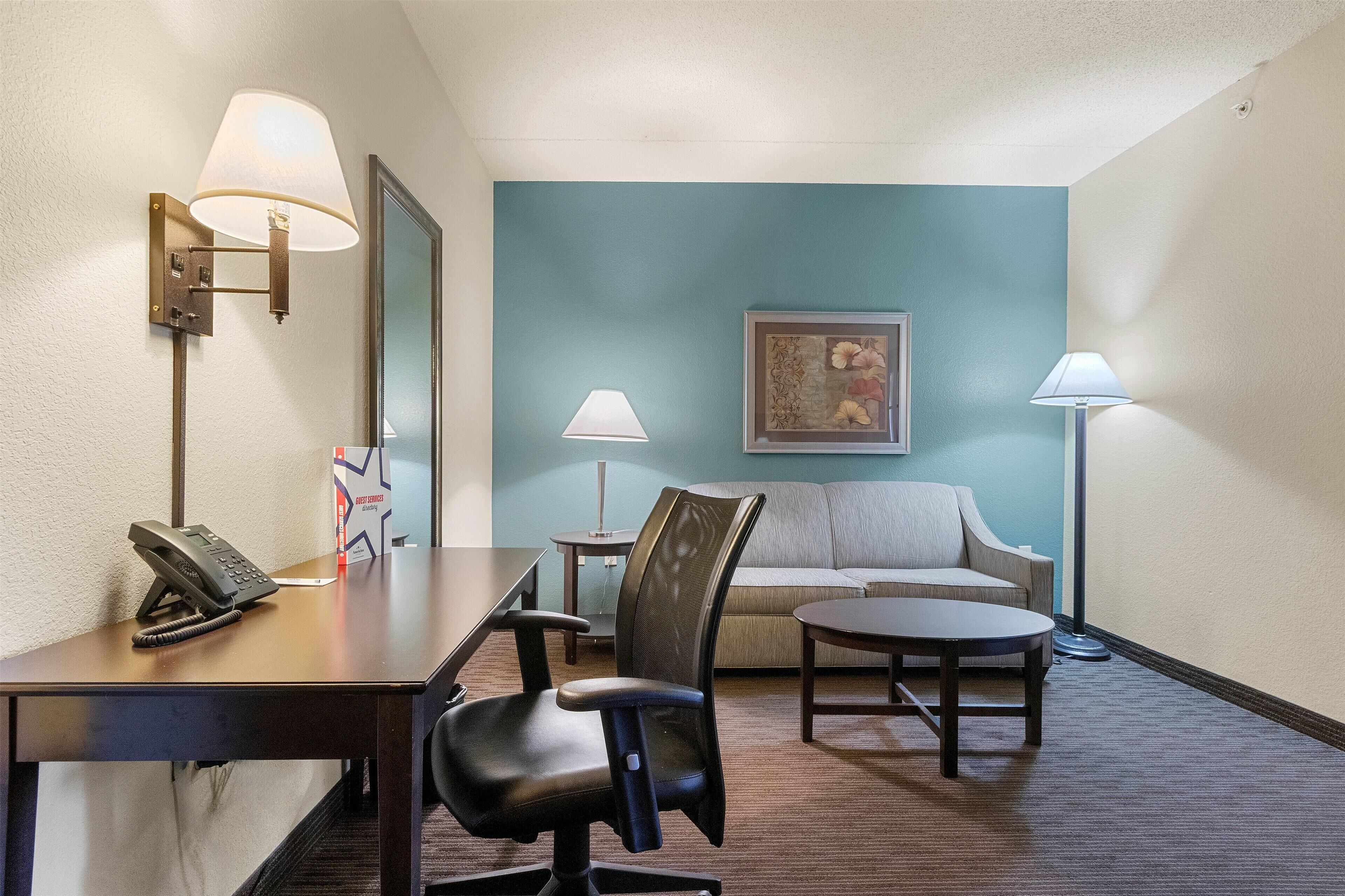 A hotel room with a desk, office chair, sofa, and two standing lamps.