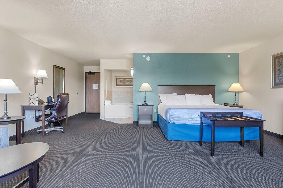 Ein Hotelzimmer mit Bett, Schreibtisch, Stuhl und einem durchgehenden Türspalt sichtbaren Badezimmer.