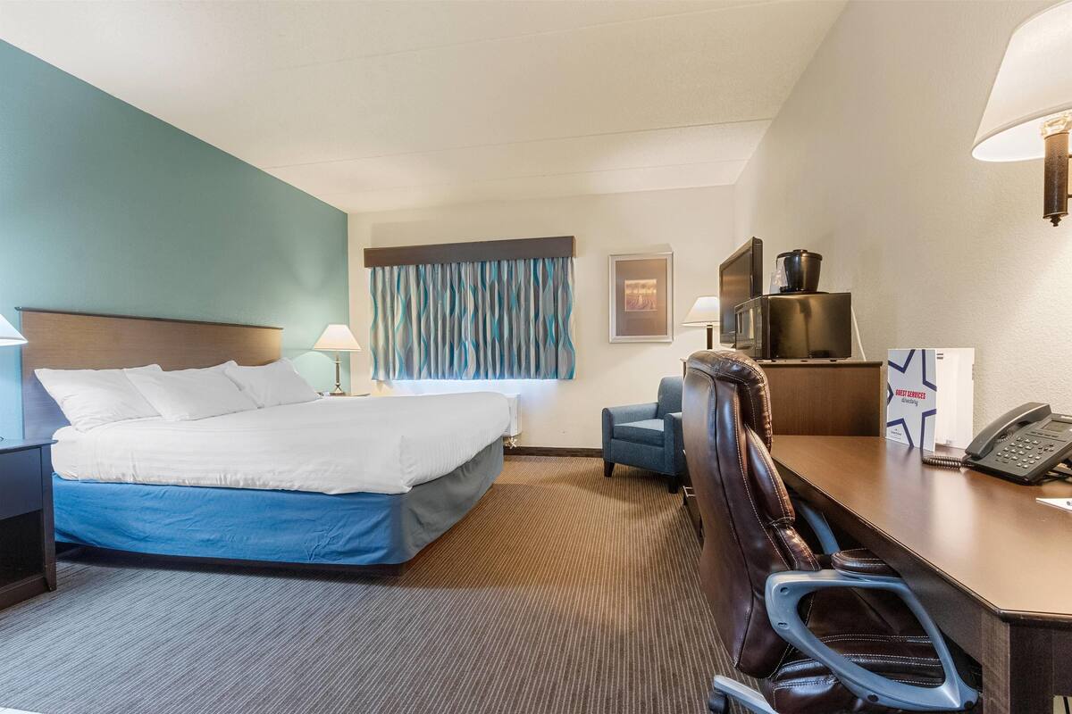 Ein Hotelzimmer mit Bett, Schreibtisch, Stuhl, Lampe und einer Mikrowelle.