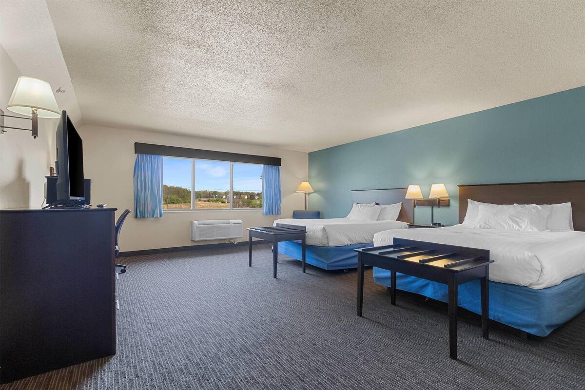Ein Hotelzimmer mit zwei Betten, einem Schreibtisch und einem Fenster mit Vorhängen.
