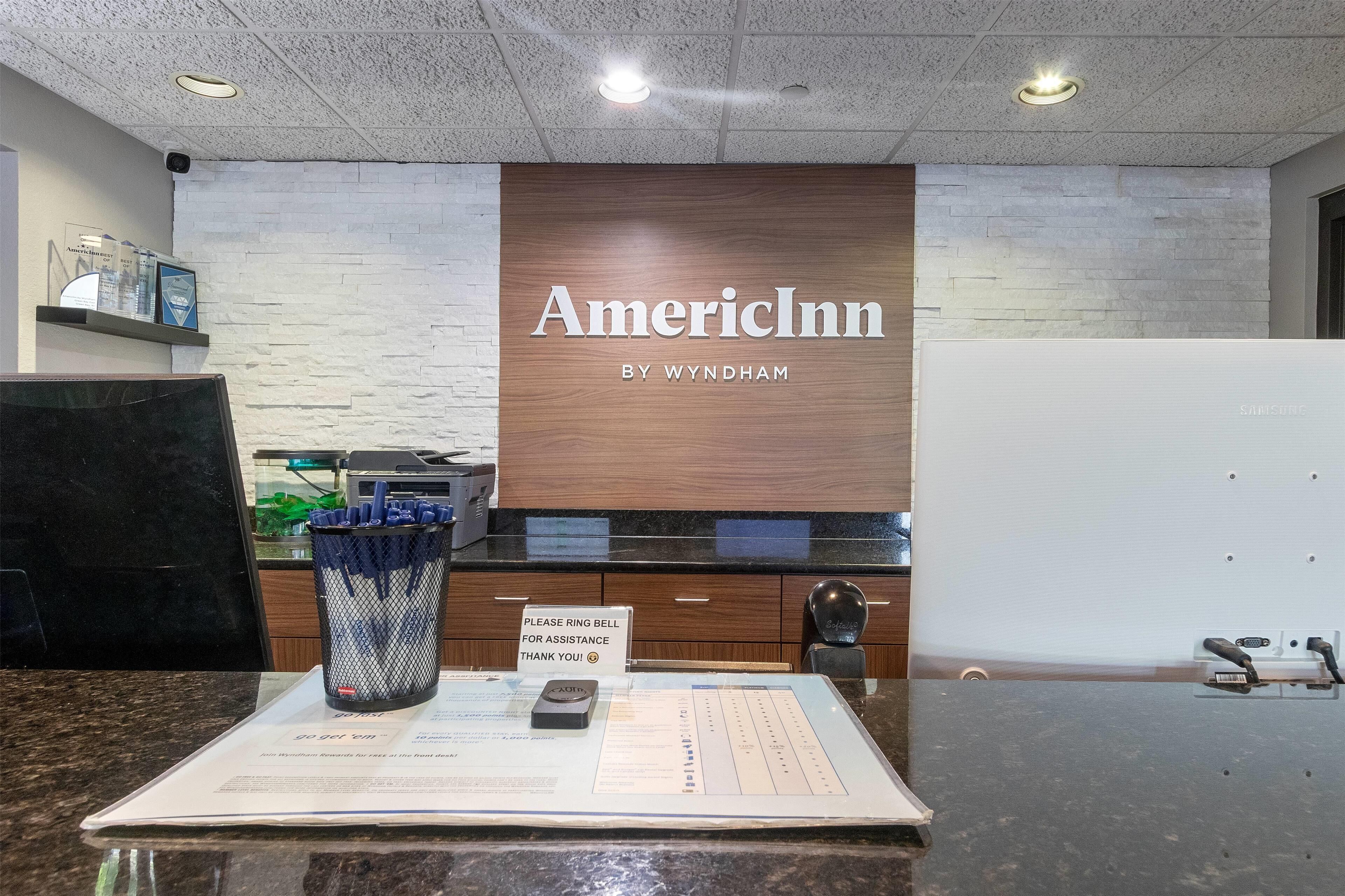 Een receptiebalie met een bord waarop 'AmerInn by Wyndham' staat en een bordje met de tekst 'Bel voor hulp'.