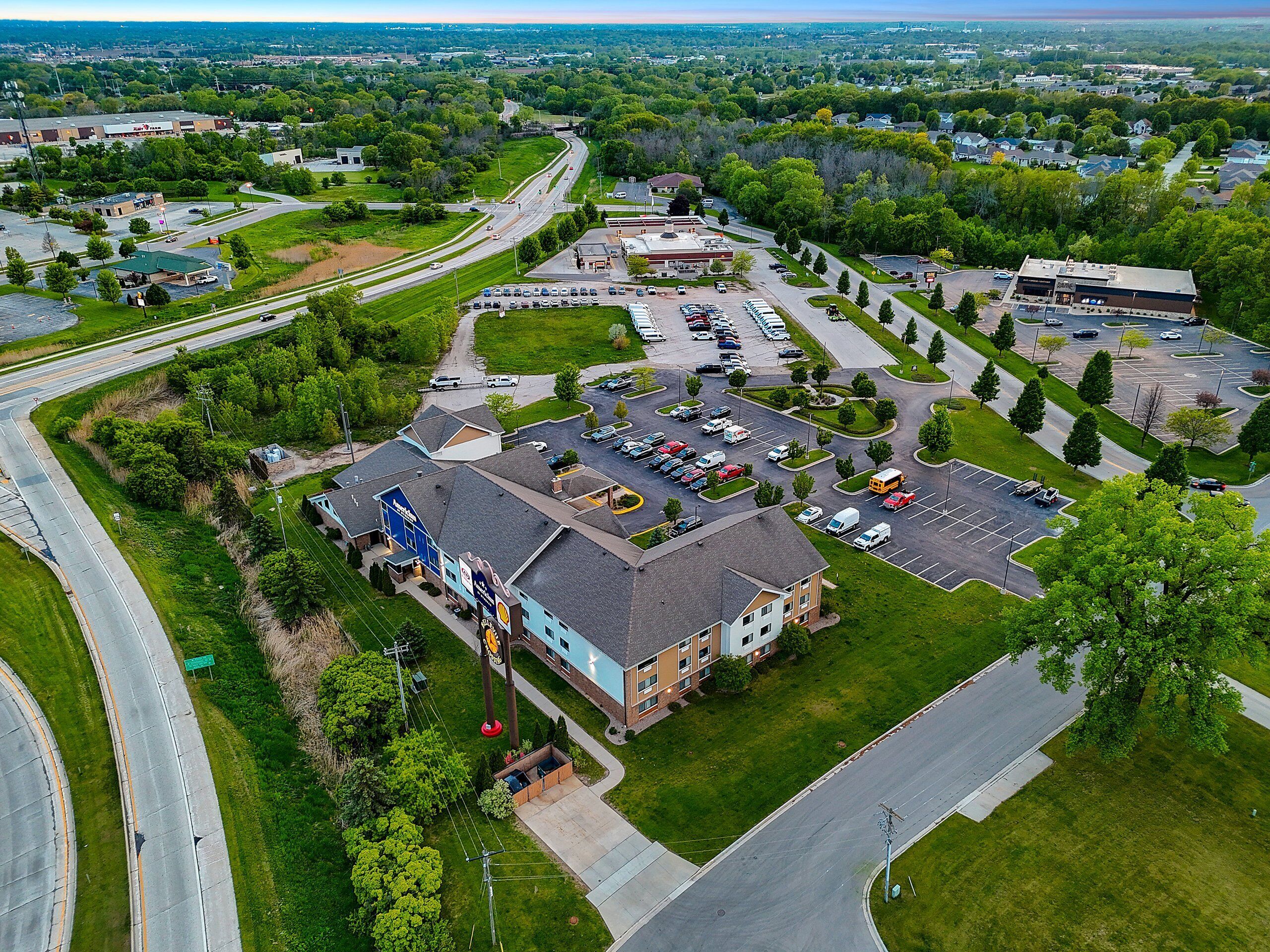 An aerial view of a commercial area with a large parking lot, a Shell gas station, and a building with a blue and white facade.