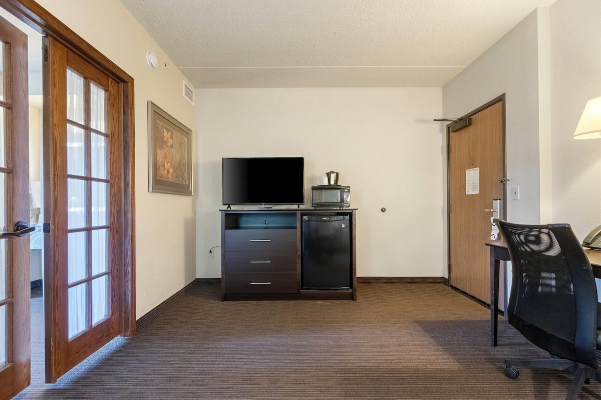 Ein Hotelzimmer mit Holztür, Schreibtisch mit Stuhl, Fernseher und kleinem Kühlschrank.
