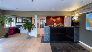 A hotel lobby with a reception desk, a large potted plant, a clock, and a map on the wall. - Canadas Best Value Inn Prince George (Prince George)
