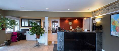 A hotel lobby with a reception desk, a large potted plant, a clock, and a map on the wall.