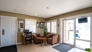 A room with a door, two armchairs, a small table, a potted plant, and a view of the outside through a glass door. - Canadas Best Value Inn Prince George (Prince George)