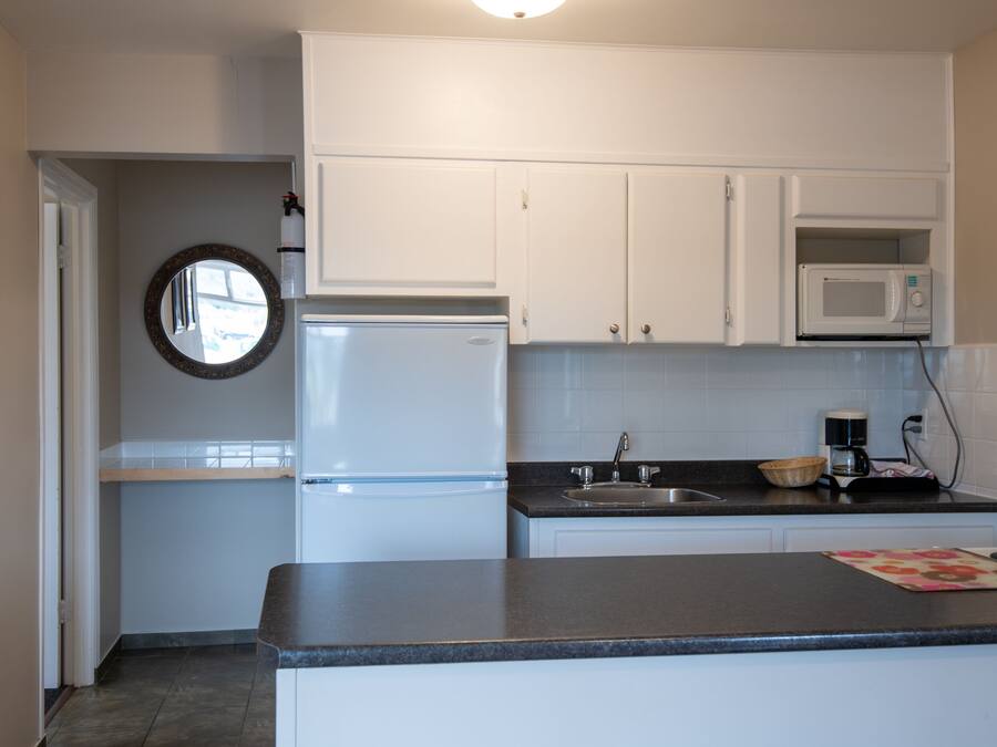 A compact kitchen with white cabinets, a white refrigerator, a microwave, a sink, and a countertop.