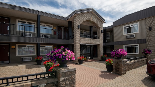 A multi-story building with a central courtyard featuring potted plants and a red car parked nearby. - Canadas Best Value Inn Prince George (Prince George)