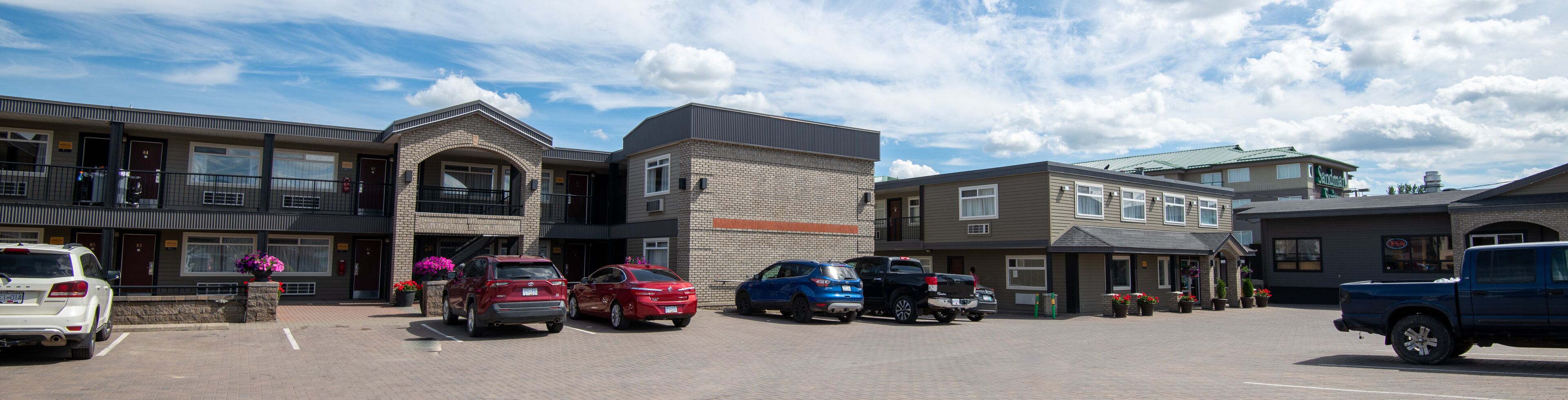 A parking lot with several cars, a building with a brick facade, and a sign that reads "Sandman."