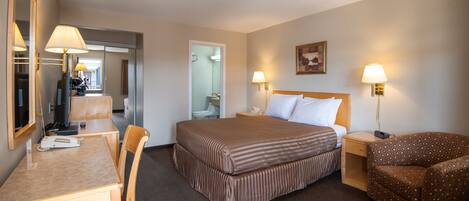 Habitación de hotel con cama, escritorio, silla, mesita de noche y espejo.
