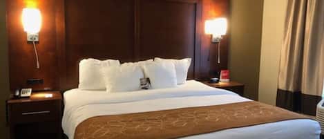 A hotel room with a large bed, two bedside tables, a nightstand, and a wall-mounted lamp.
