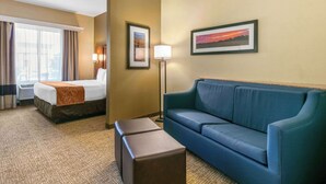 A hotel room with a bed, a blue sofa, a lamp, and framed pictures on the wall.