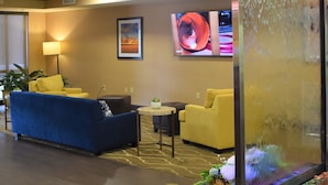 A hotel lobby with a blue sofa, yellow armchairs, a flat-screen TV, and a decorative water feature.