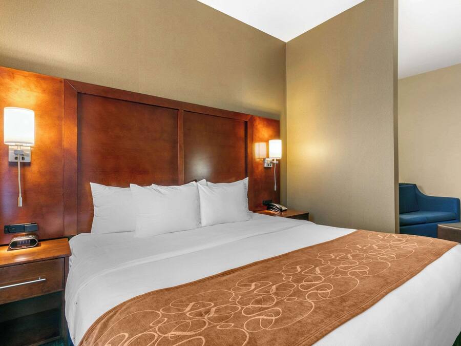 Habitación de hotel con una cama grande, cabecero de madera, mesitas de noche y una silla azul.