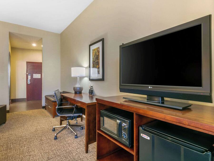 A hotel room with a large flat-screen TV, a desk with a chair, a lamp, a microwave, and a mini fridge.
