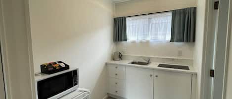 A compact kitchen with white cabinets, a built-in microwave, a sink, and a window with curtains.