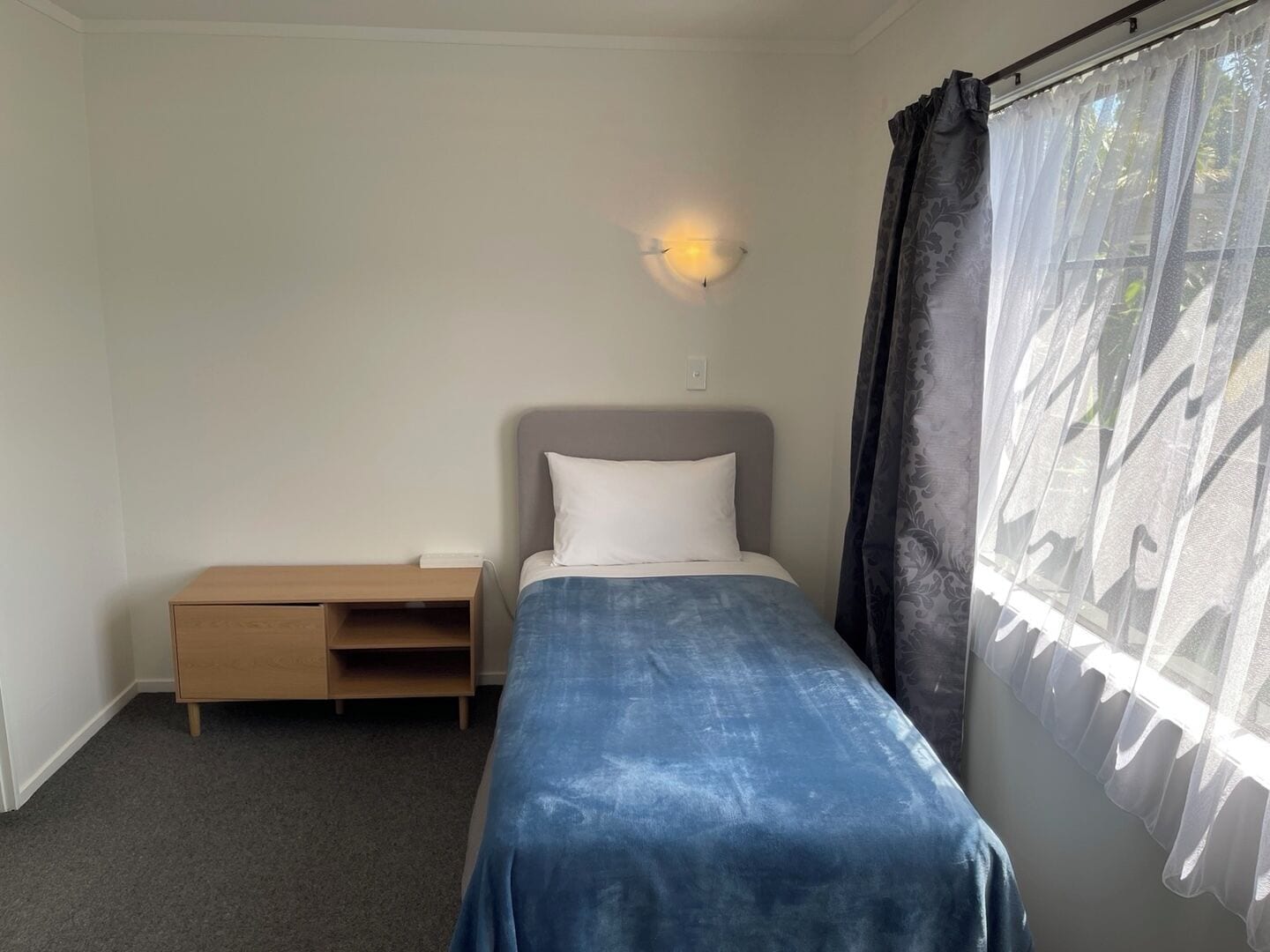 Una cama individual con cabecera, mesita de noche y lámpara de pared.