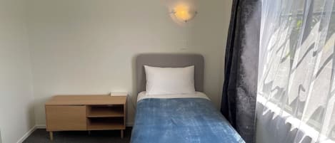 Una cama individual con cabecera, mesita de noche y lámpara de pared.