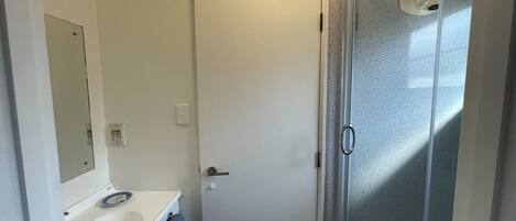 A small bathroom with a white sink, mirror, and a glass shower enclosure.