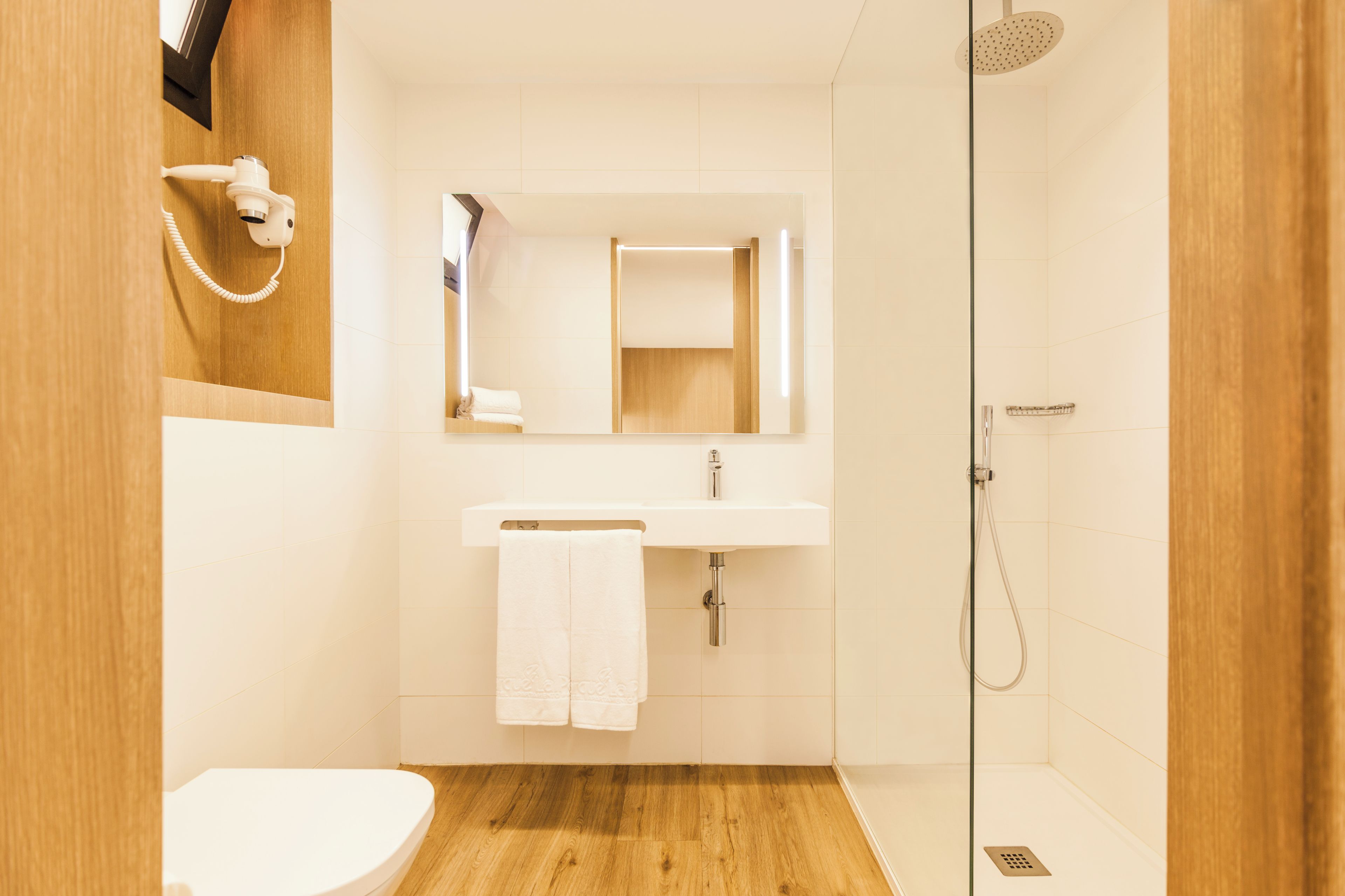 Une salle de bain moderne avec un plancher en bois, des accessoires blancs, un lavabo avec un miroir et une douche.