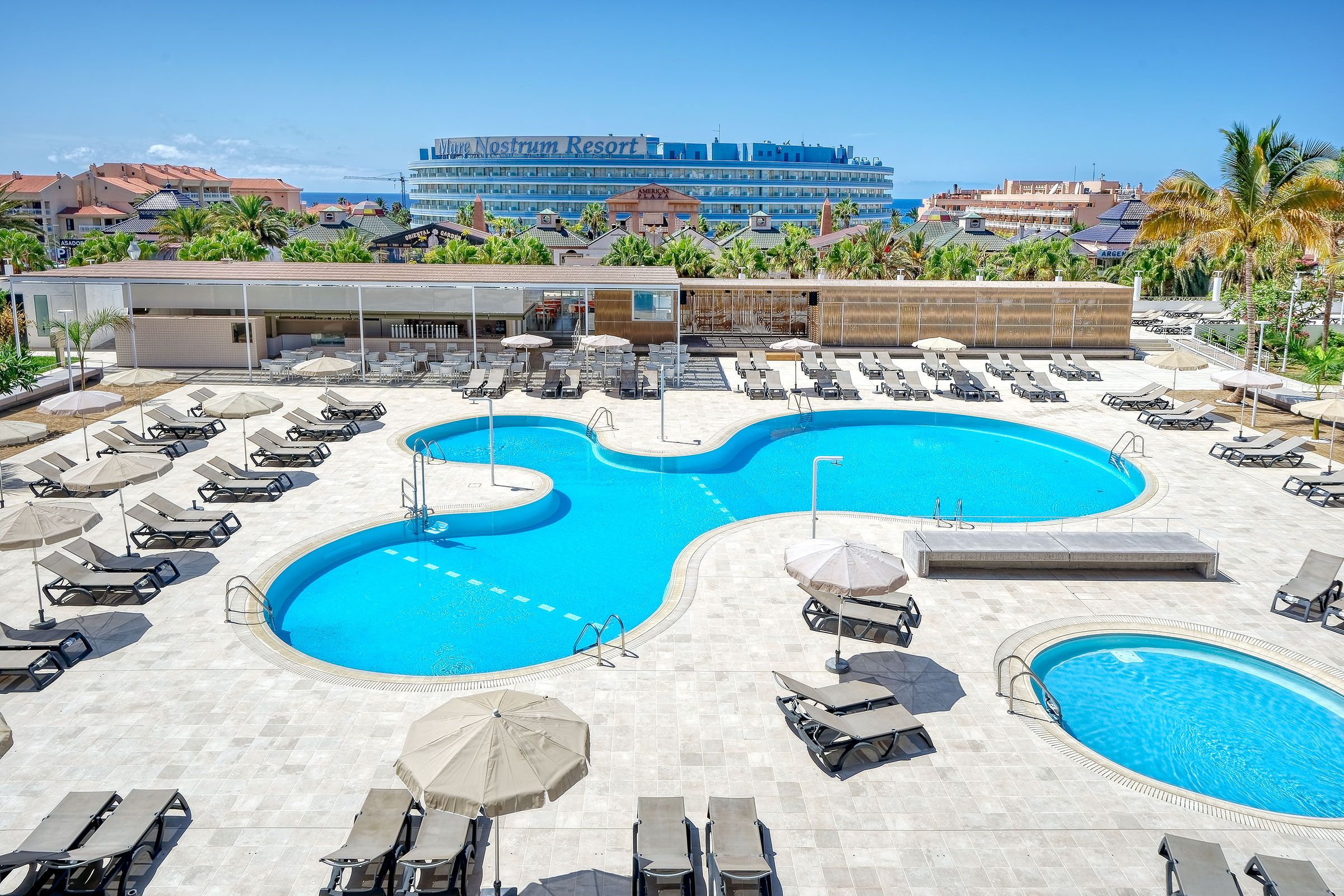 A resort with a large central pool, multiple smaller pools, and a variety of sun loungers and umbrellas.
