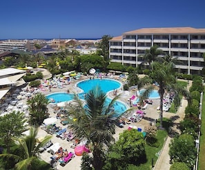Resort com várias piscinas, espreguiçadeiras e palmeiras.