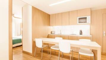 A modern kitchen with a white countertop, wooden cabinets, and a microwave. There are four white chairs around the table.