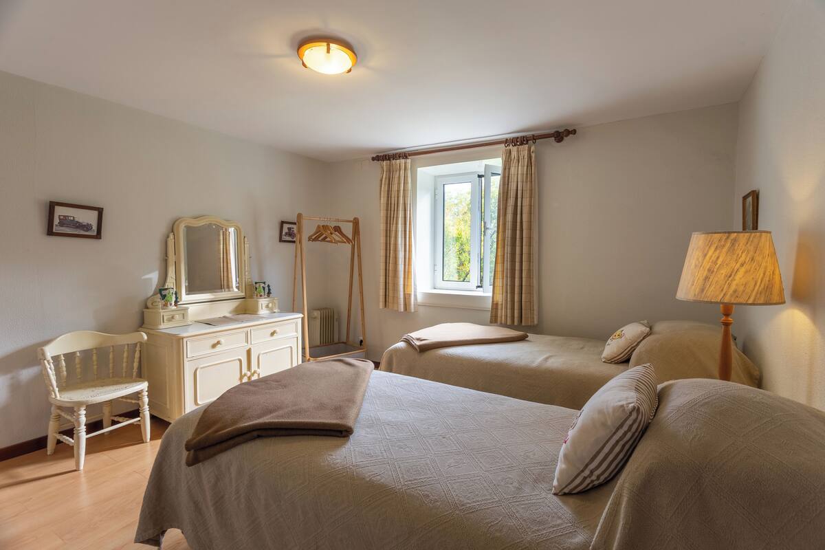 A bedroom with two beds, a dresser, a chair, a mirror, and a window with curtains.