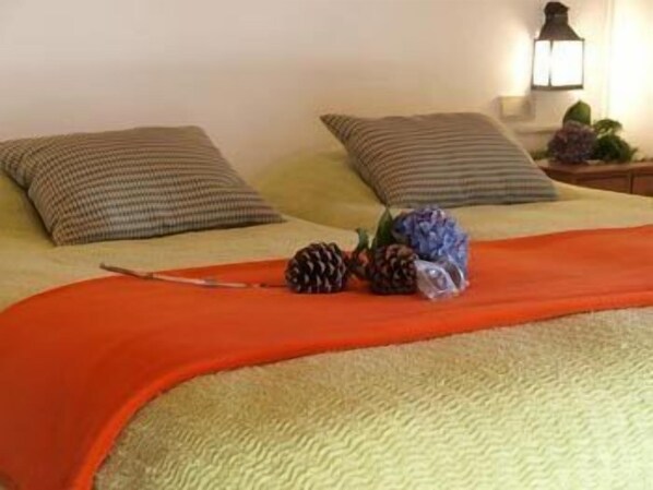 Una cama bien hecha con un edredón verde con textura, dos almohadas a rayas y una manta roja.