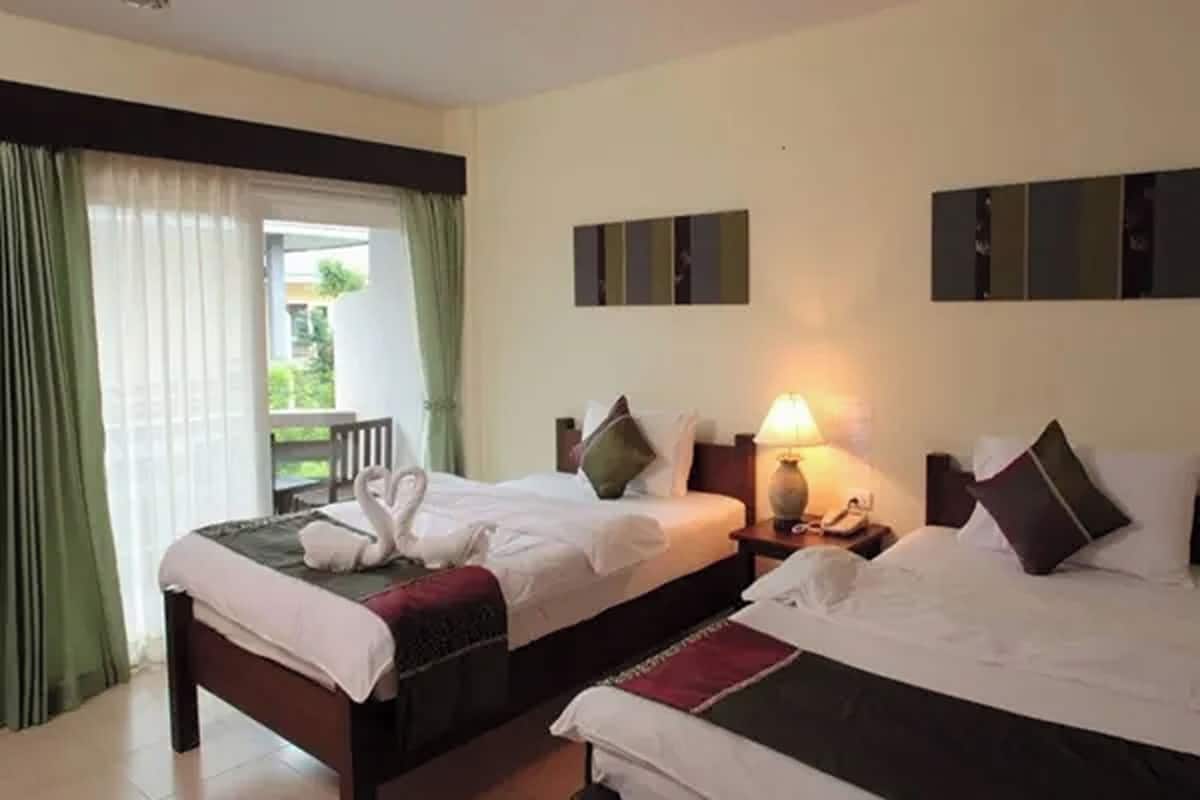 A hotel room with two beds, a balcony, and a view of greenery.