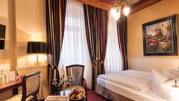 A hotel room with a bed, a desk with a lamp, a chair, and a painting on the wall.