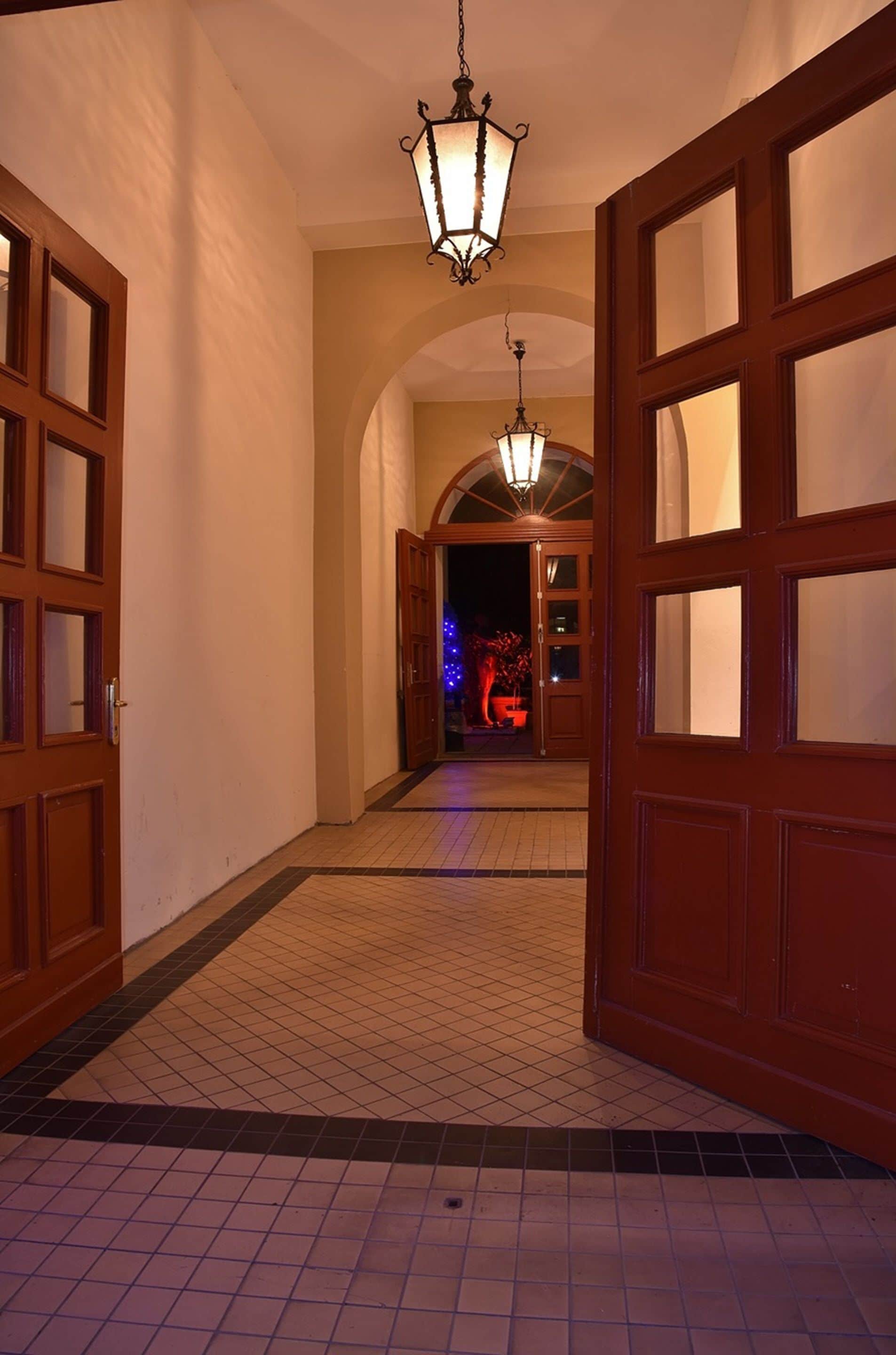A hallway with wooden doors, a tiled floor, and a hanging light fixture.