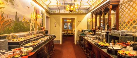 A buffet area with various food stations, a chandelier, and a mural on the wall.