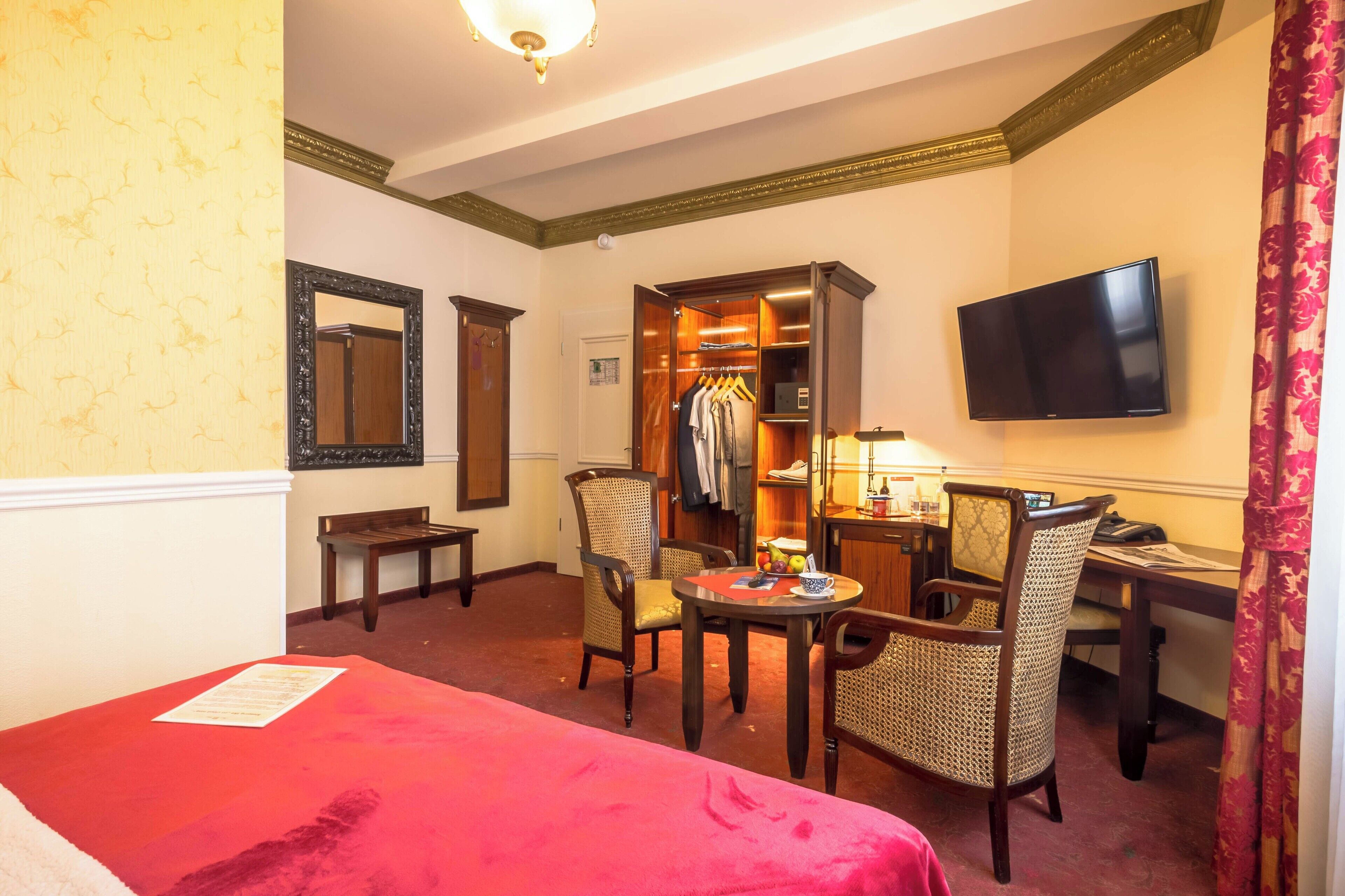 Una habitación de hotel con cama, escritorio, silla, armario, televisor y espejo.
