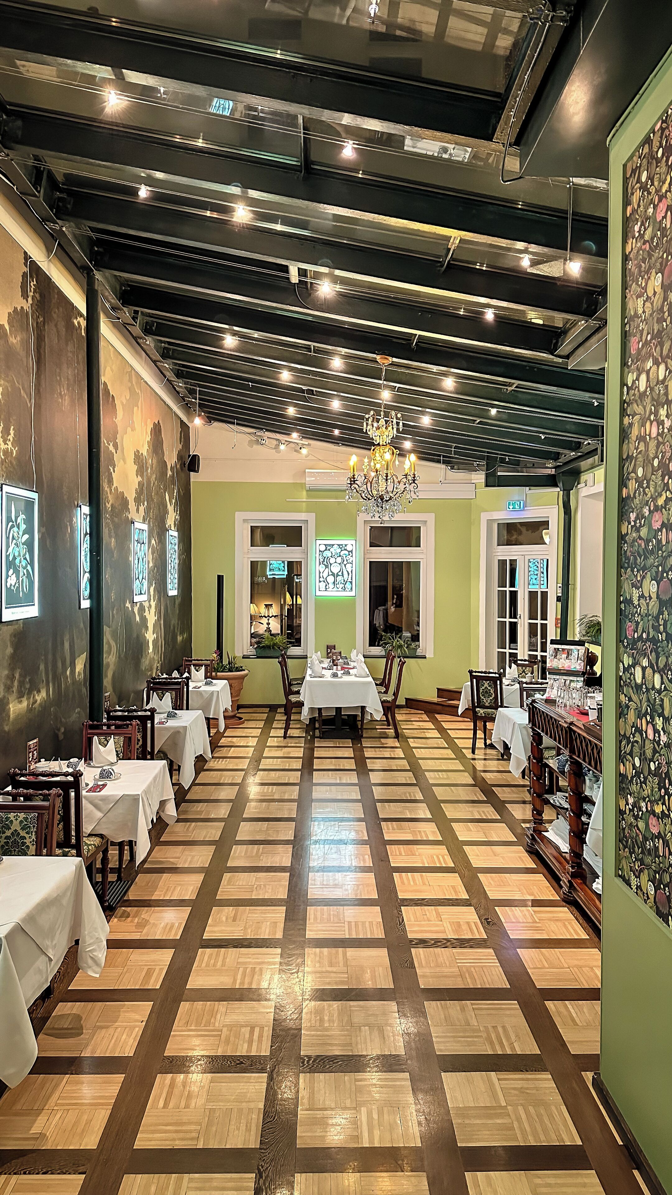 A restaurant with a central dining area, multiple tables, and a chandelier.