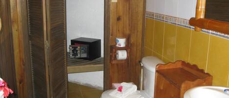 A bathroom with a toilet, a wooden shelf with toiletries, and a sink.